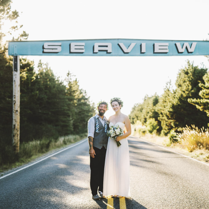 Bride and groom in flower crowns pose on the road beneath the vintage Seaview highway sign